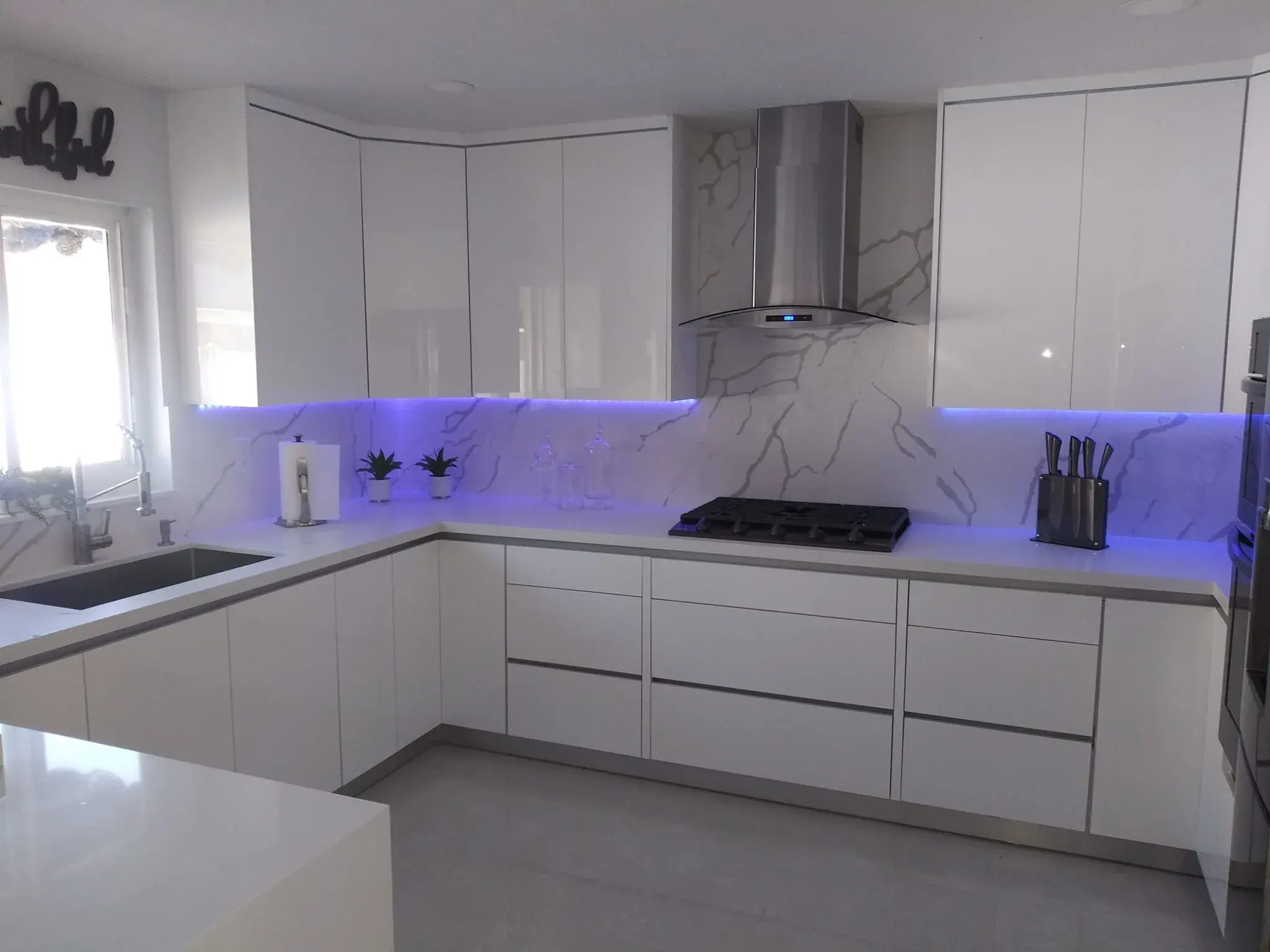 White high-gloss kitchen with a range hood and LED under-cabinet lighting