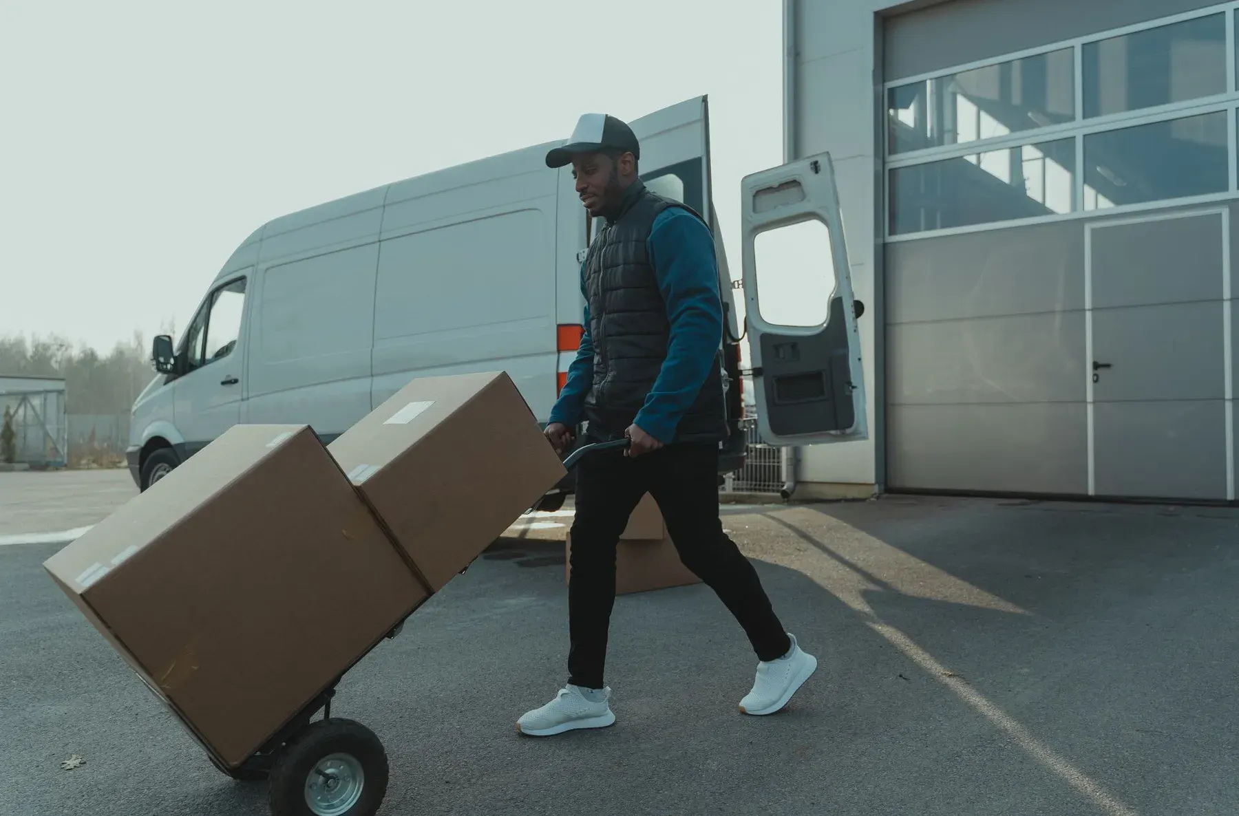 Worker moving stacked boxes on a hand truck beside a delivery van