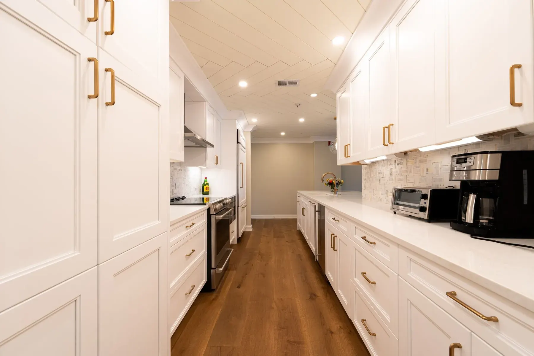 Long galley kitchen with white cabinets and gold hardware in a remodeled home